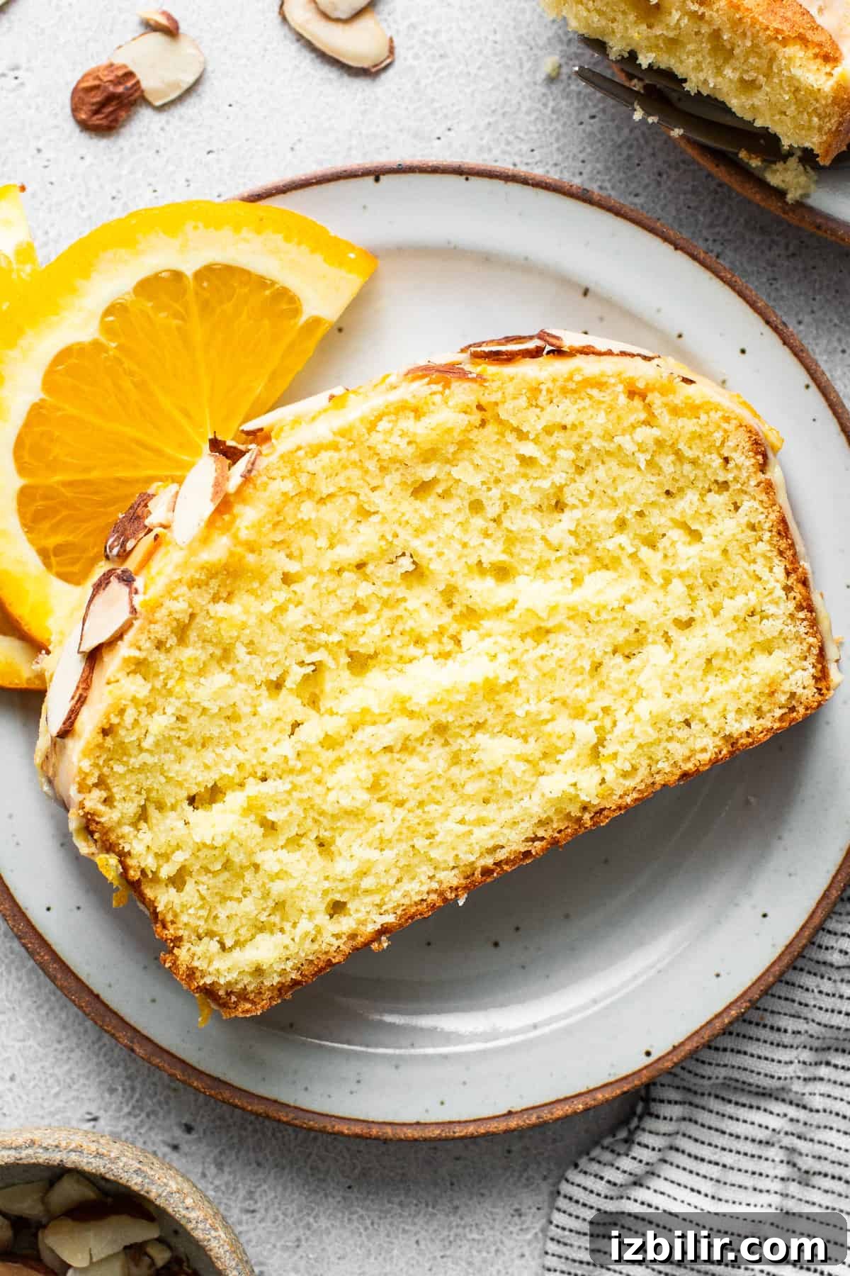 Zesty Orange Cake Recipe with Citrus Glaze 6 A slice of orange cake with almonds on a plate.