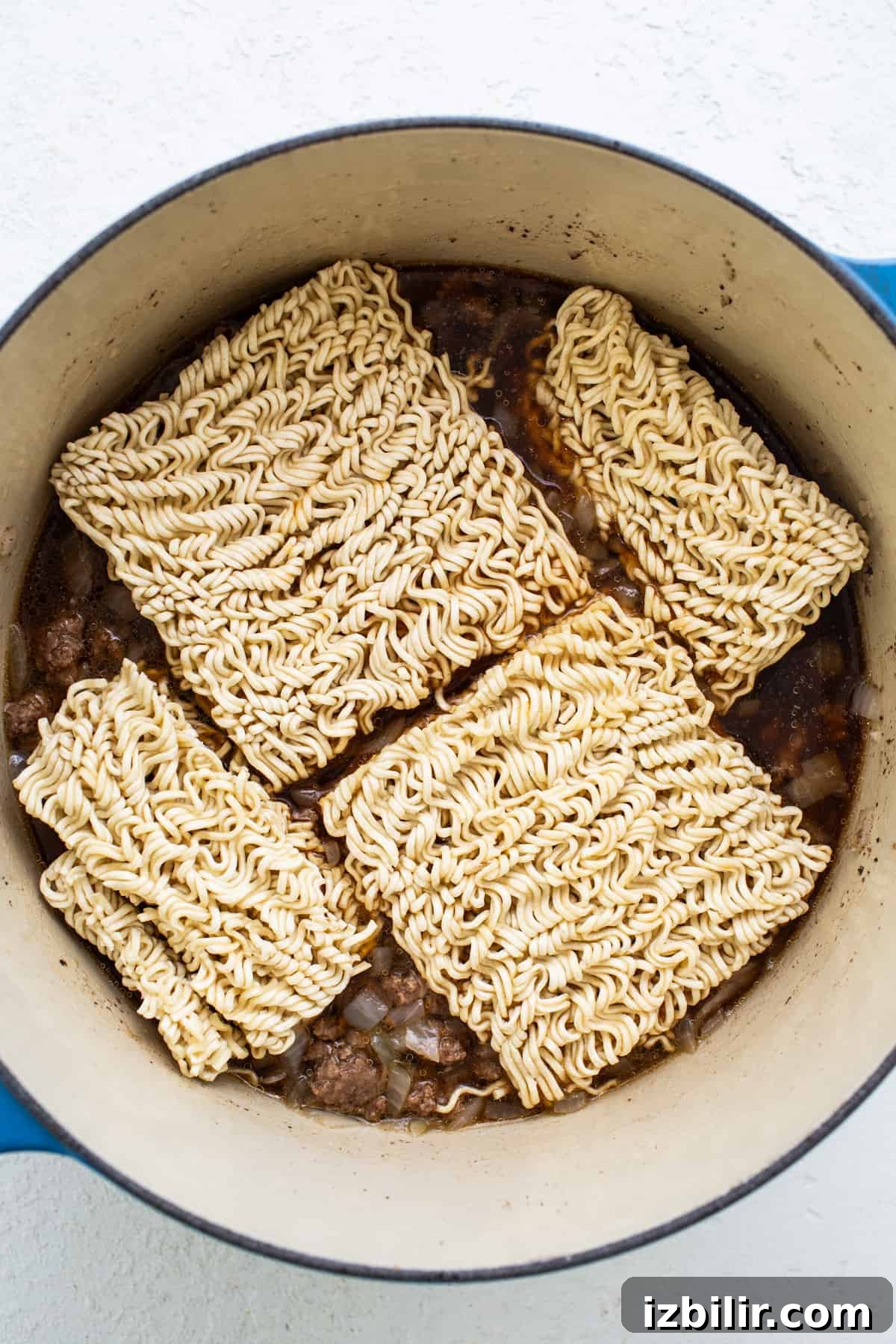 Ramen noodles in a pot on a white surface.