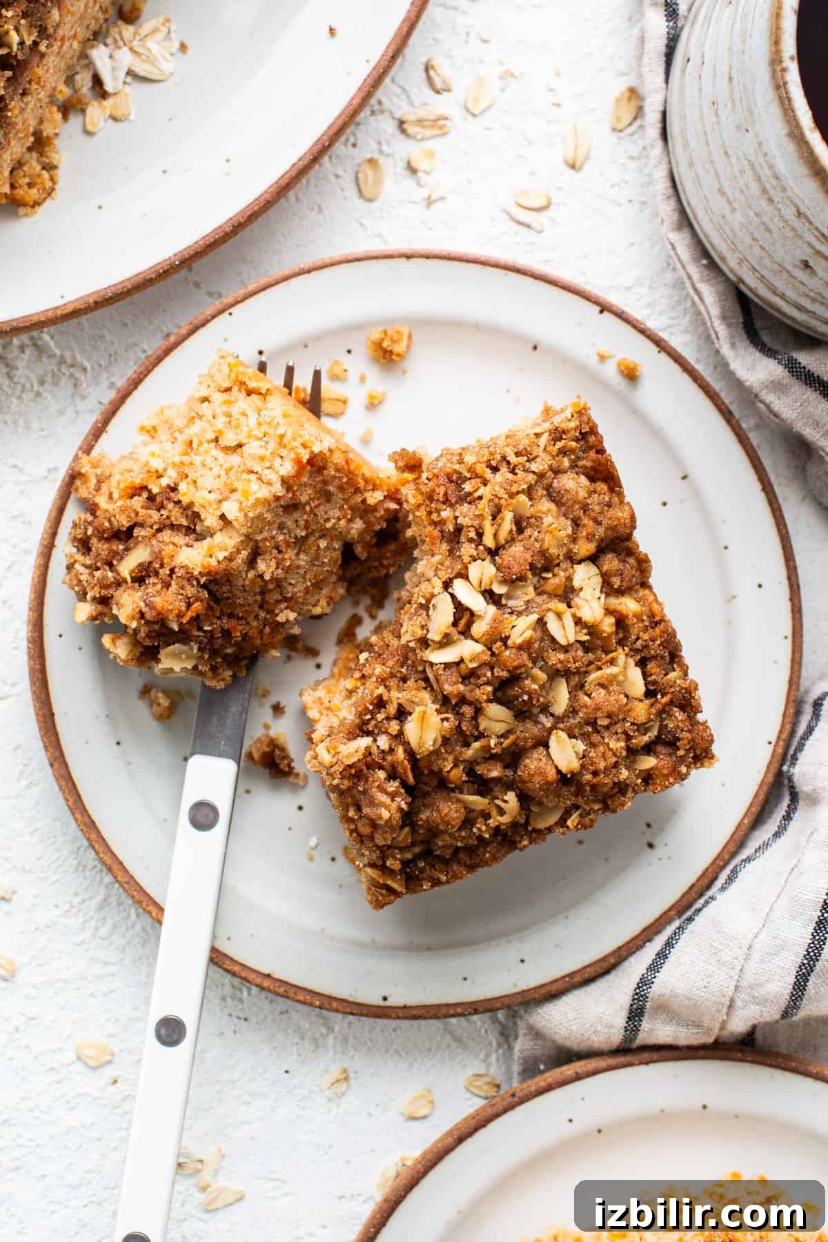 Spiced Carrot Coffee Cake with Cream Cheese Glaze 6 A slice of oatmeal cake on a plate next to a cup of coffee.