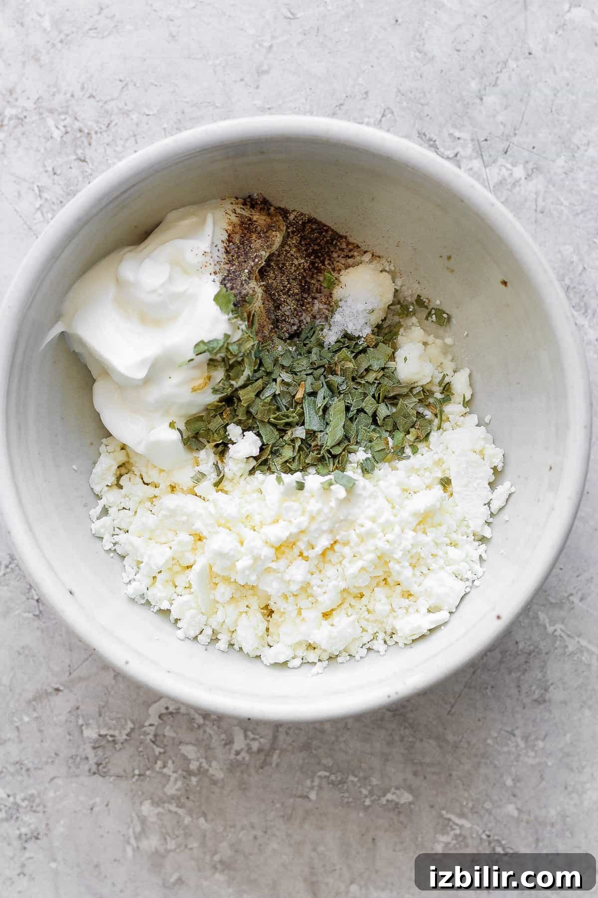A bowl of crumbled feta cheese mixed with seasonings and yogurt on a textured surface.