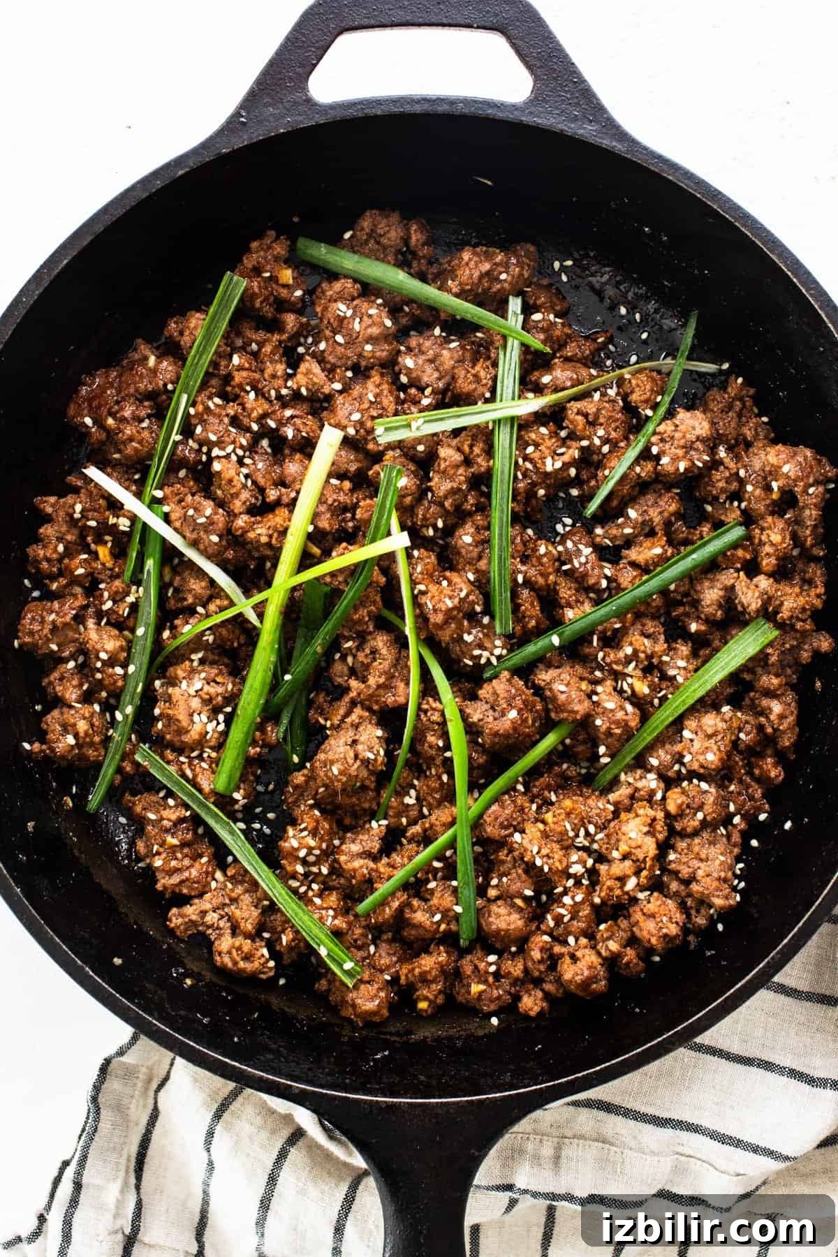 Cooked Korean ground beef garnished with green onions and sesame seeds in a cast iron skillet.