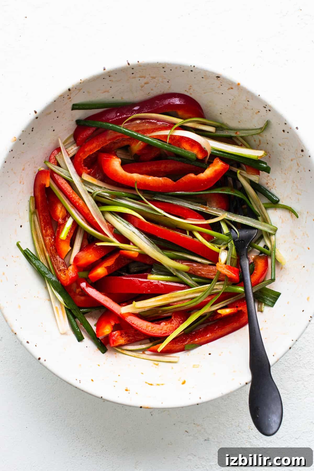 A bowl of sliced red bell peppers and green beans ready for cooking with Korean ground beef, accompanied by a spoon.