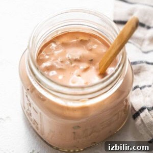 Classic Homemade Thousand Island Dressing Recipe 6 A jar of creamy homemade thousand island dressing with a wooden spoon.