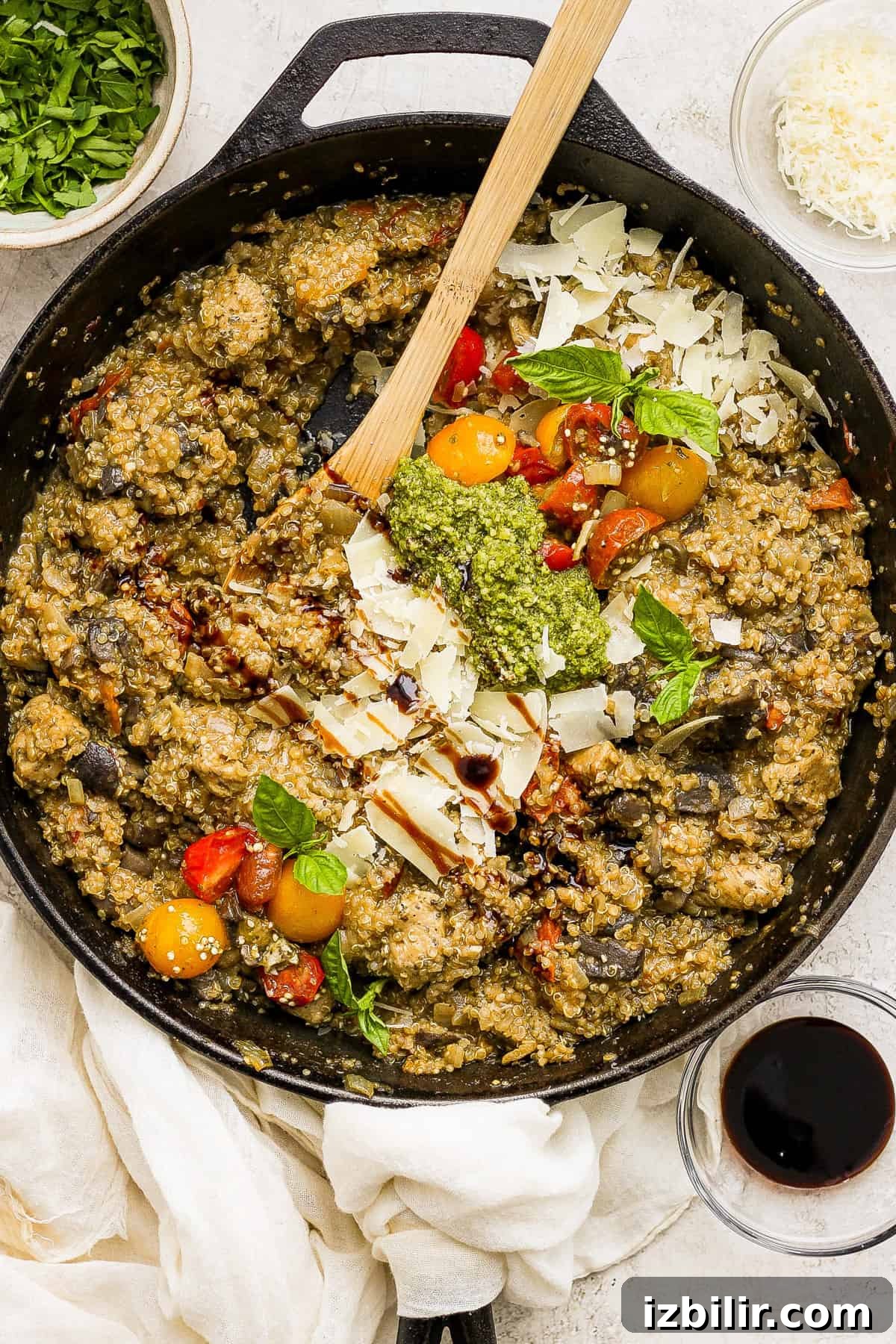 One-Pot Pesto Chicken and Quinoa Skillet Recipe 2 A skillet full of vegetables and herbs with a wooden spoon.