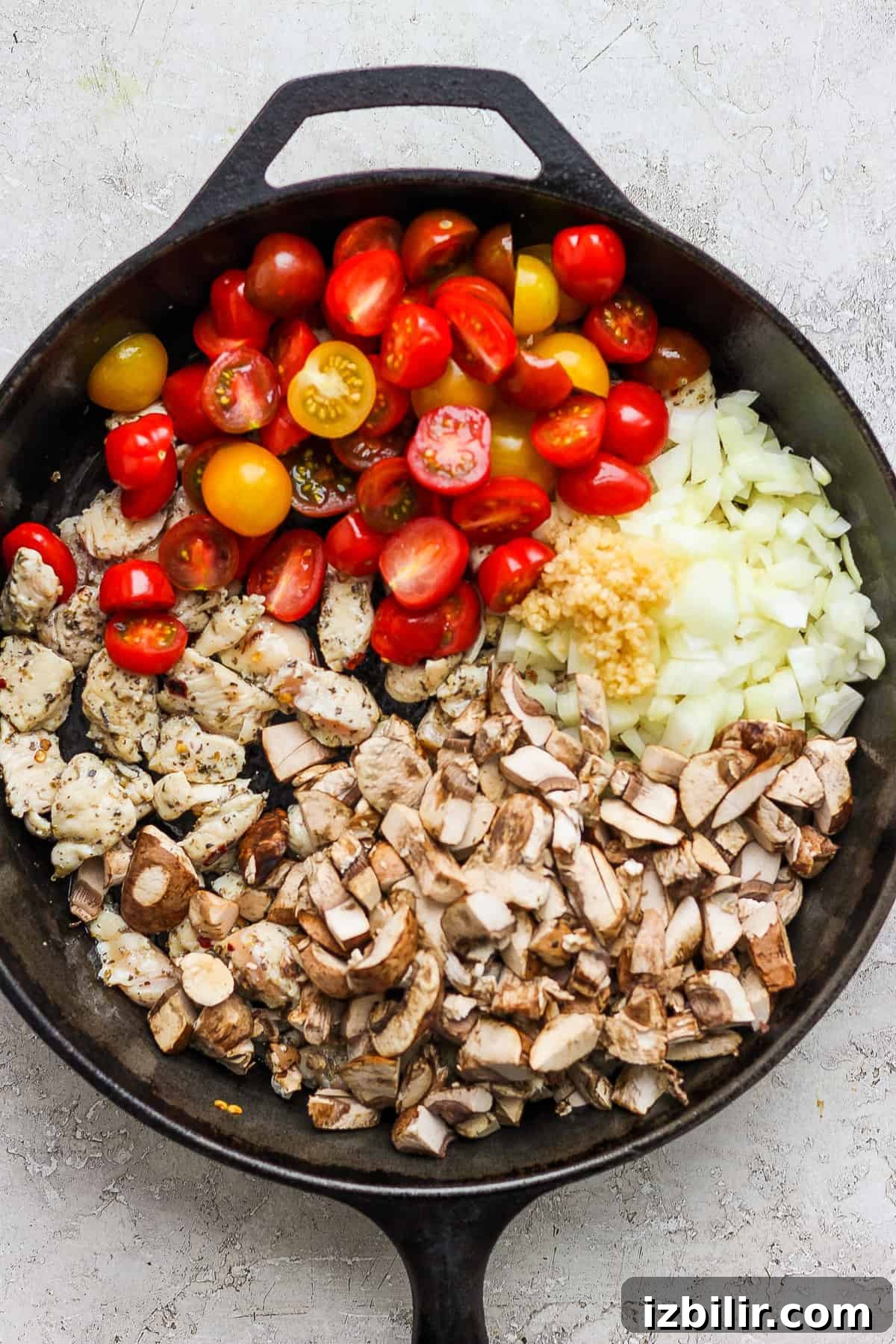One-Pot Pesto Chicken and Quinoa Skillet Recipe 4 A frying pan with tomatoes, onions, and mushrooms.