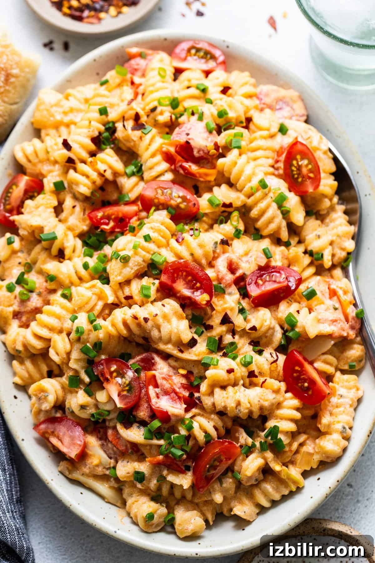 A plate of creamy pasta with sliced cherry tomatoes and chopped green onions
