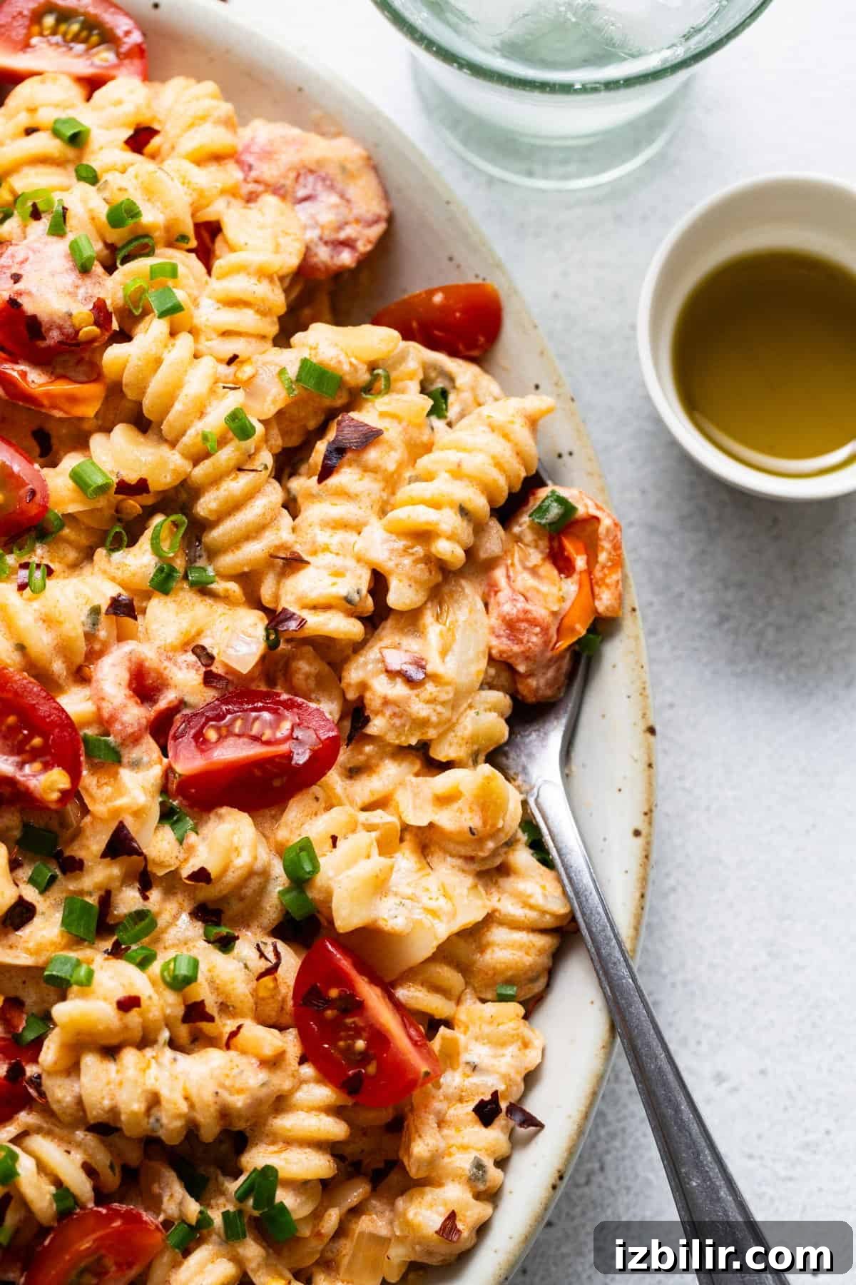 A dish of creamy pasta with sliced sausage, cherry tomatoes, and garnished with chopped green onions
