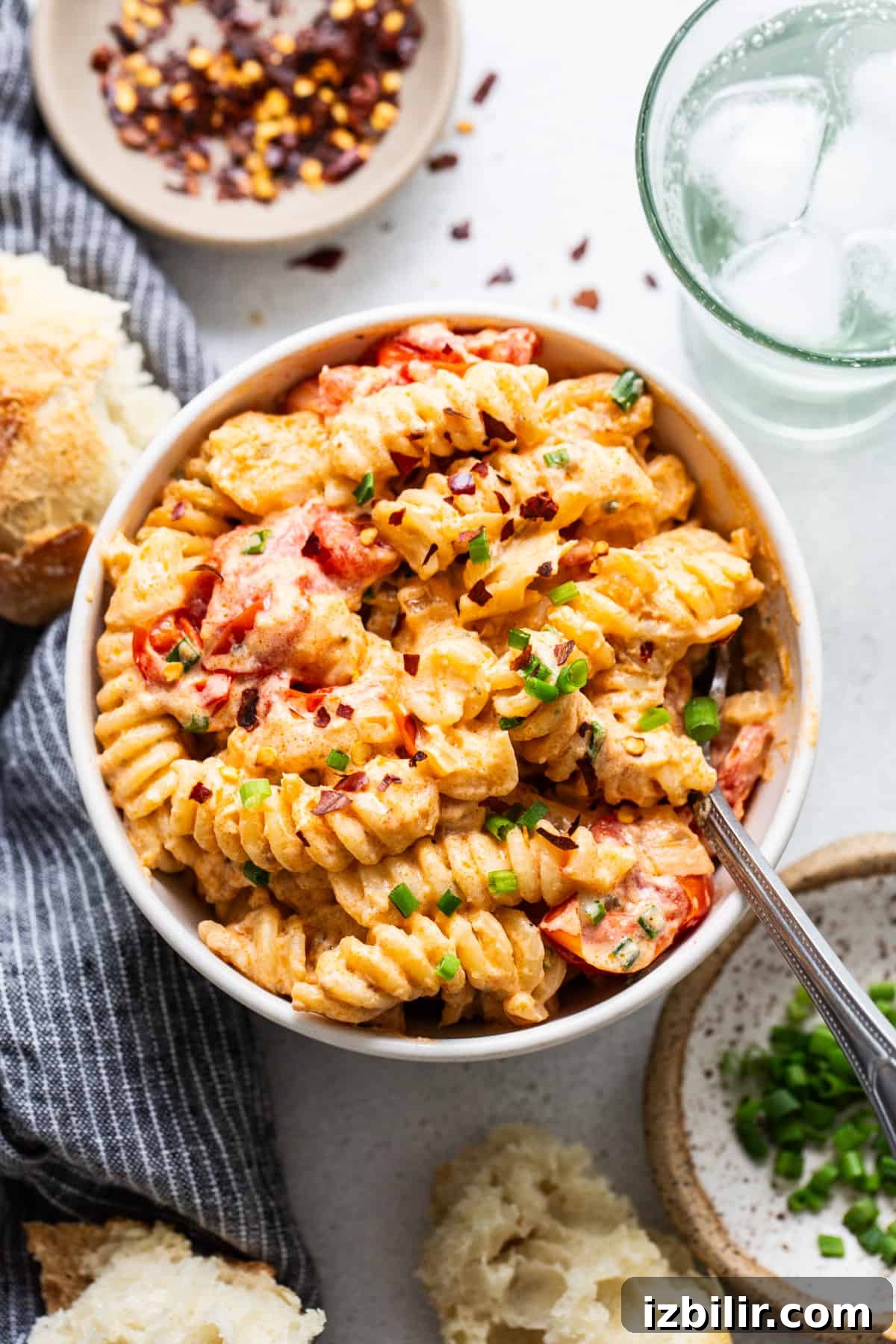A bowl of creamy tomato pasta garnished with green onions, served with bread