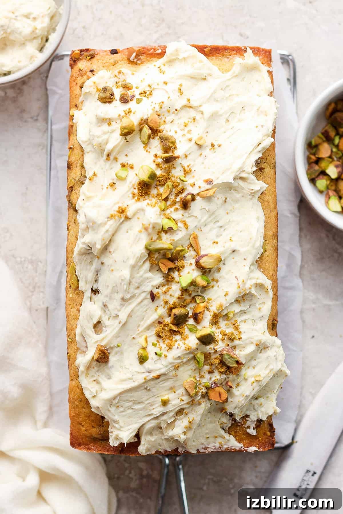 Vanilla Pistachio Loaf Recipe with Pistachio Frosting 5 A freshly baked loaf cake topped with a creamy white frosting and sprinkled with chopped pistachios.