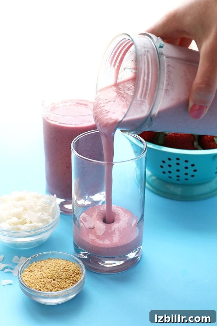 Hand pouring post-workout coconut strawberry smoothie from blender to glass