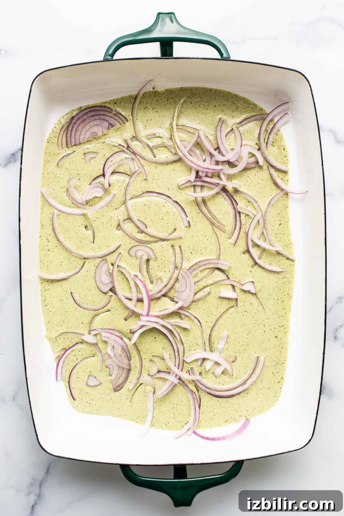 A ceramic dish containing a creamy mixture topped with thinly sliced red onions.