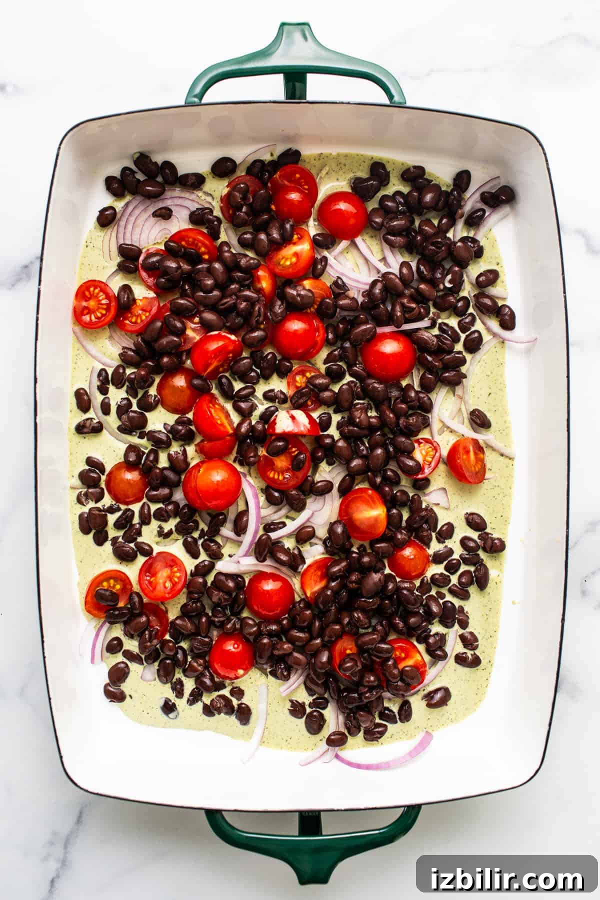 A baking dish with black beans, cherry tomatoes, and sliced onions, ready for cooking.