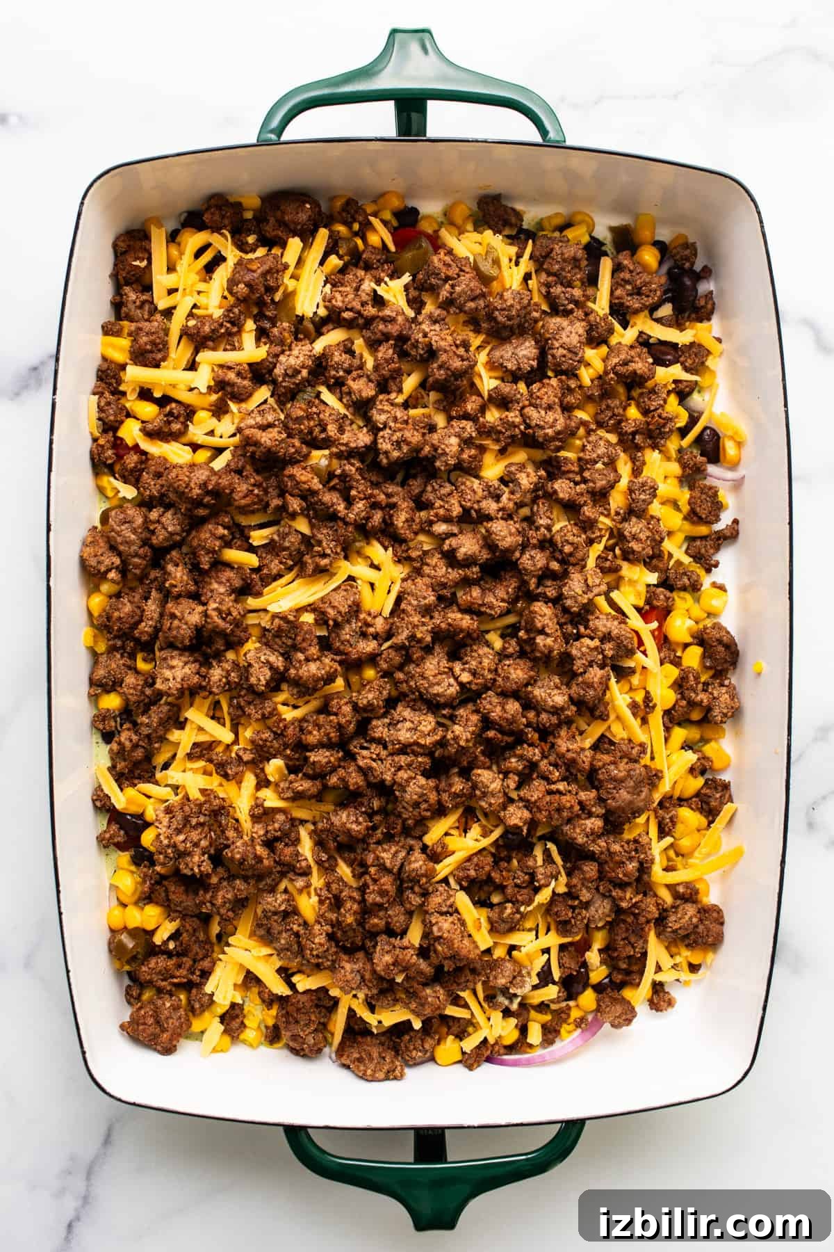 A baking dish with layers of ground beef, corn, and shredded cheese.
