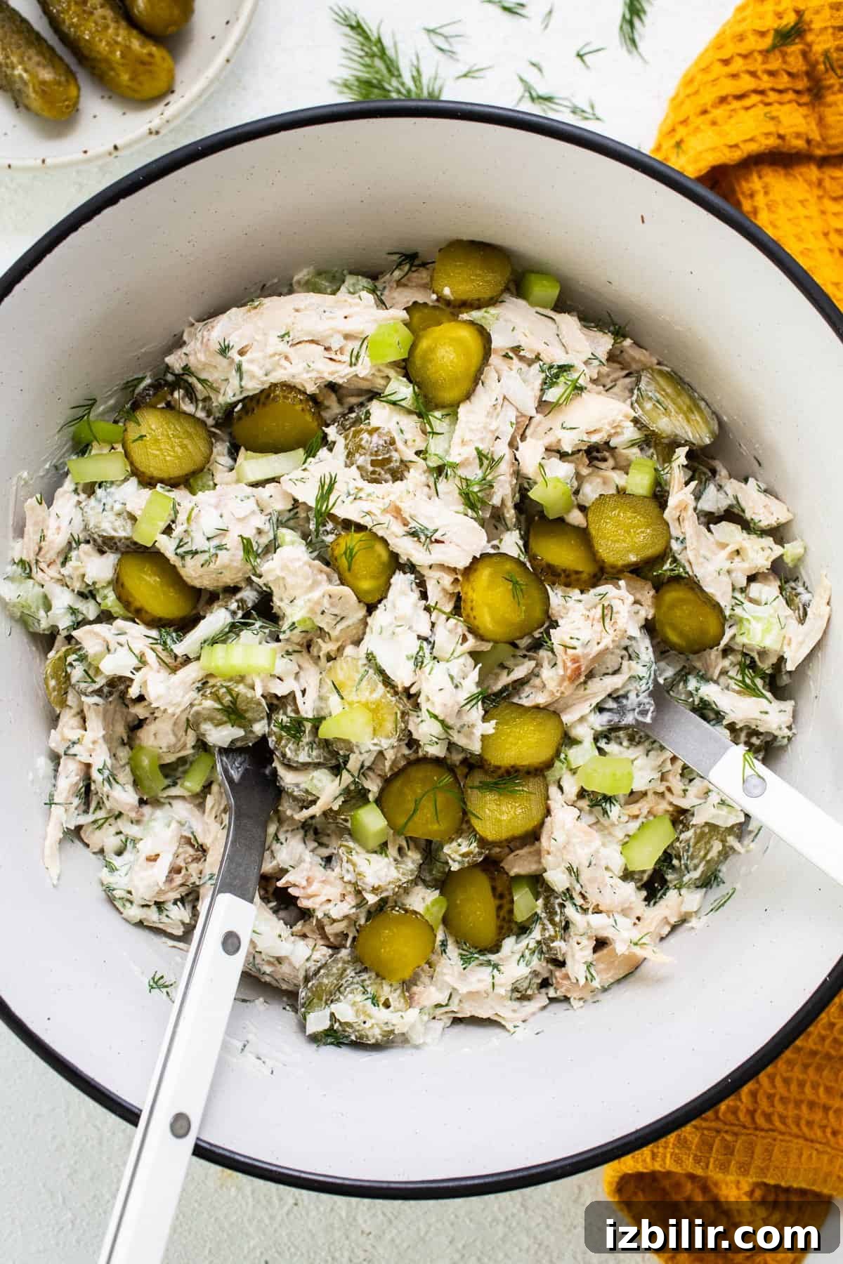 Tangy Dill Pickle Chicken Salad Recipe 5 A bowl of dill pickle chicken salad with sliced pickles and fresh dill, accompanied by serving utensils.