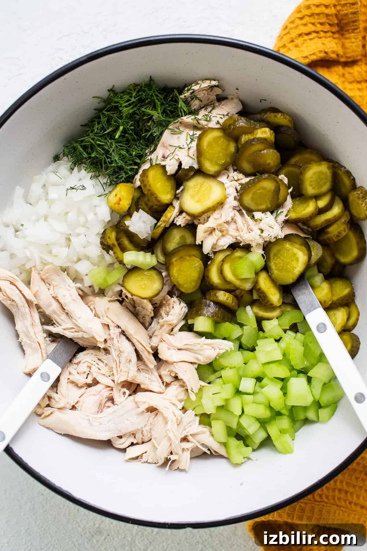 Fit Foodie Cooking Club April 2024 Classes and Recipes 3 Ingredients for a recipe including shredded chicken, chopped onions, sliced pickles, and diced celery in a bowl with tongs.