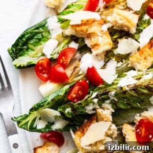 Grilled caesar salad with chicken, cherry tomatoes, croutons, and shaved parmesan cheese on a white plate.