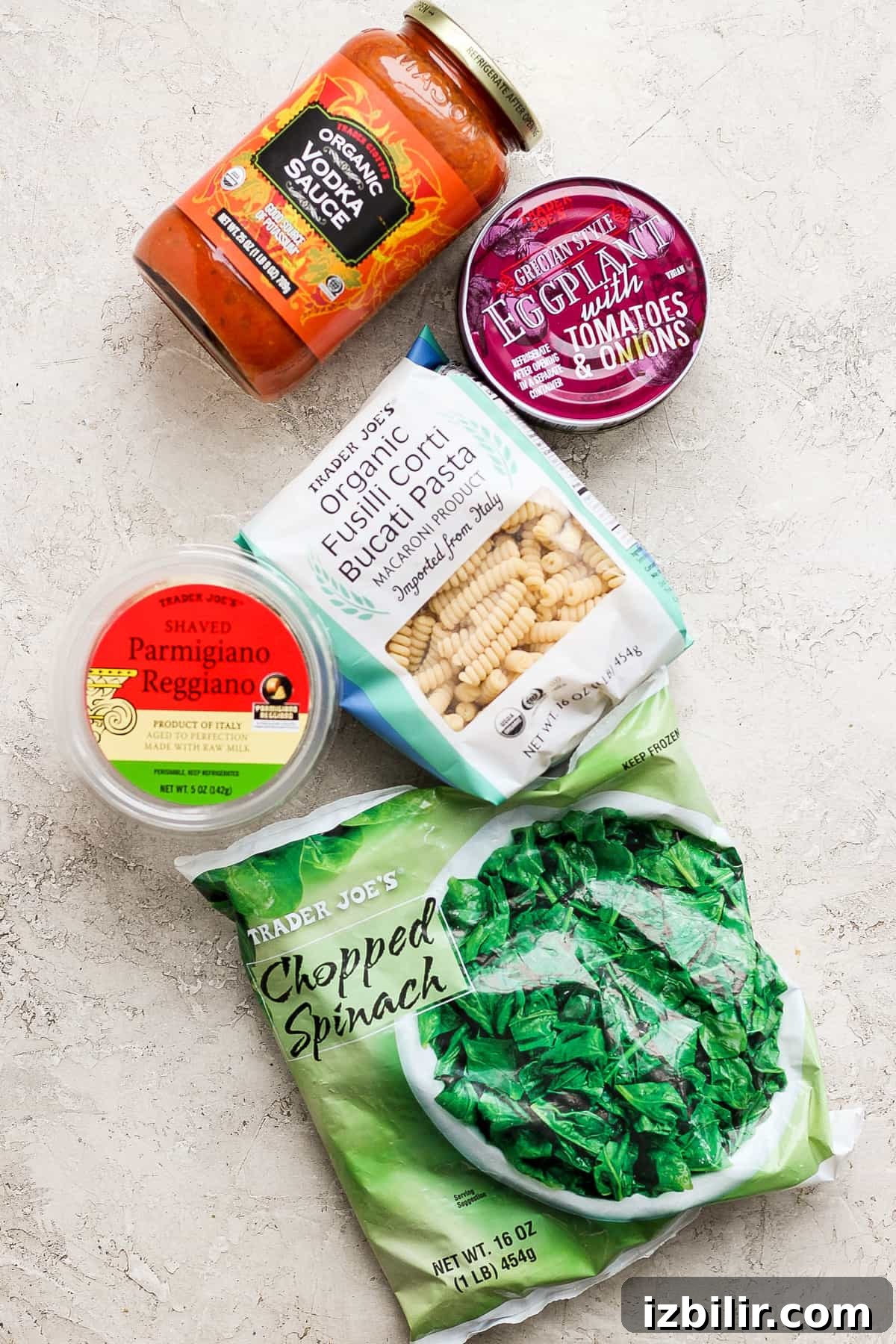 Creamy One-Pot Vodka Pasta Recipe 3 Assorted grocery items including tomato sauce, crushed tomatoes, gnocchi, parmesan cheese, and chopped spinach arranged on a light surface.