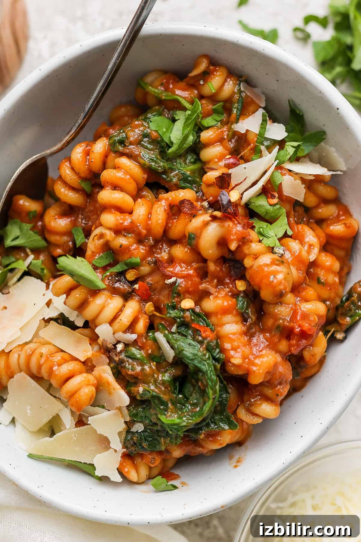 Creamy One-Pot Vodka Pasta Recipe 6 A bowl of fusilli pasta mixed with tomato sauce, spinach, and topped with shaved parmesan cheese.