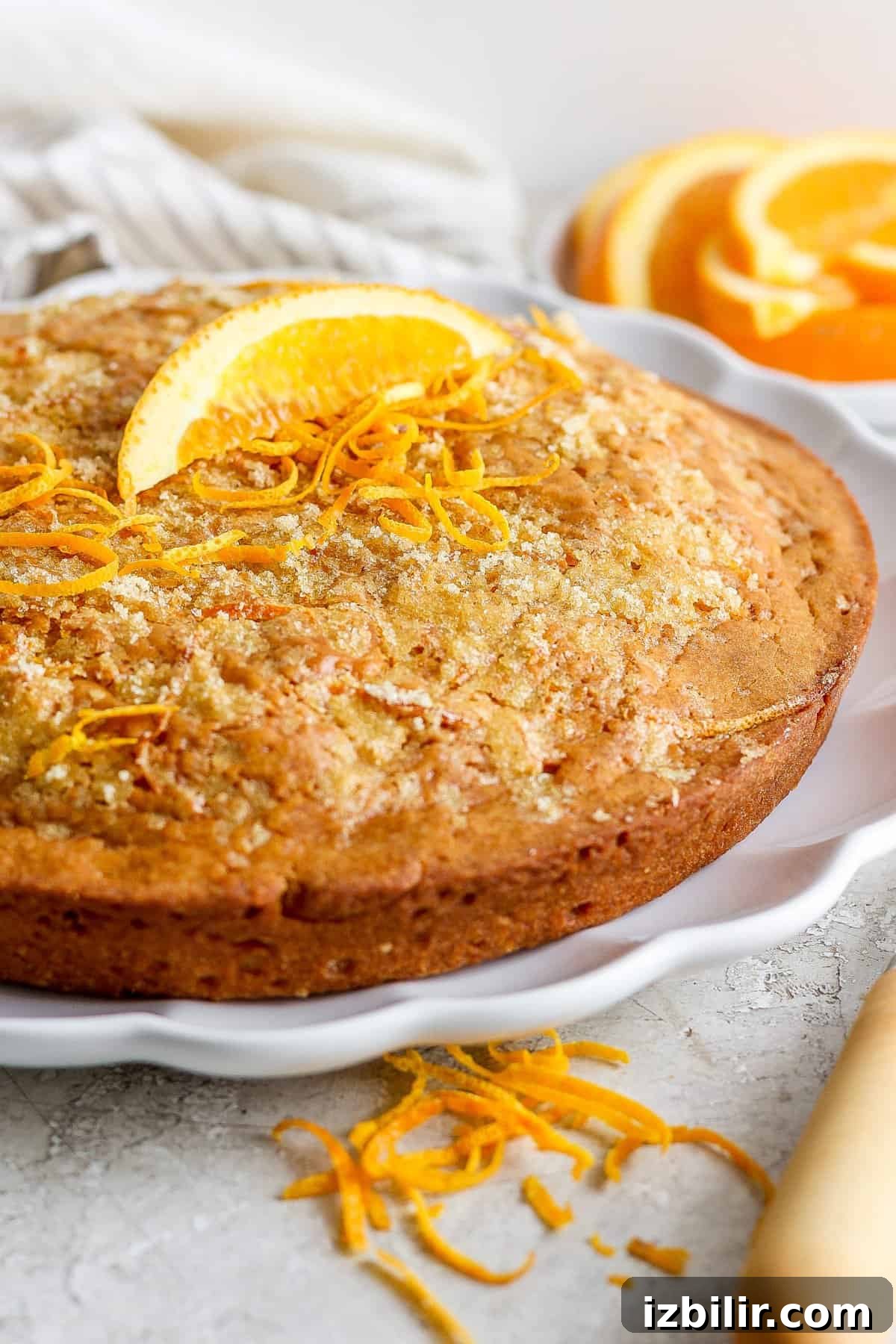 A freshly baked orange cake garnished with orange zest on a white plate.