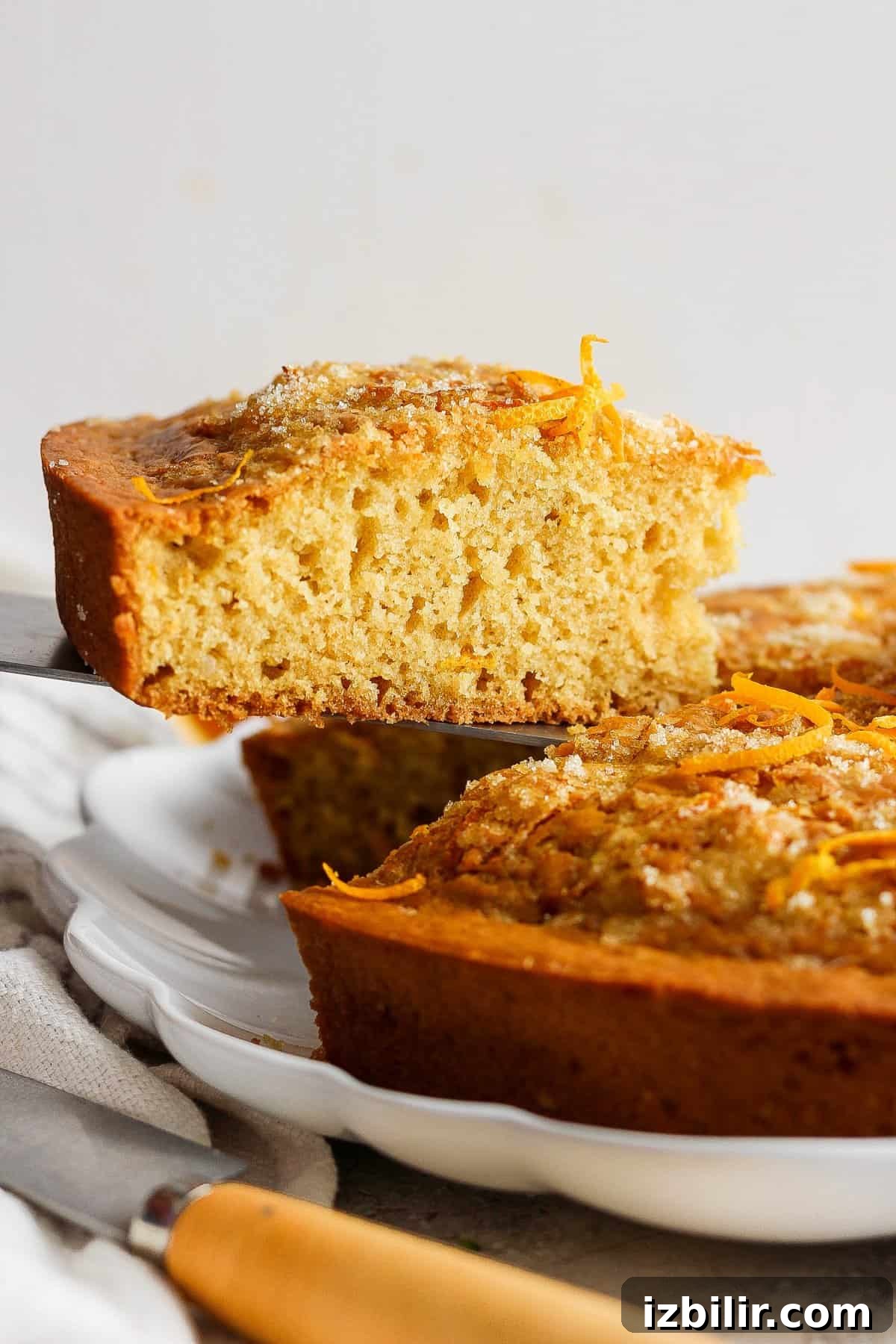 A freshly baked orange cake with a slice partially lifted out, showcasing its moist crumb and topped with orange zest.