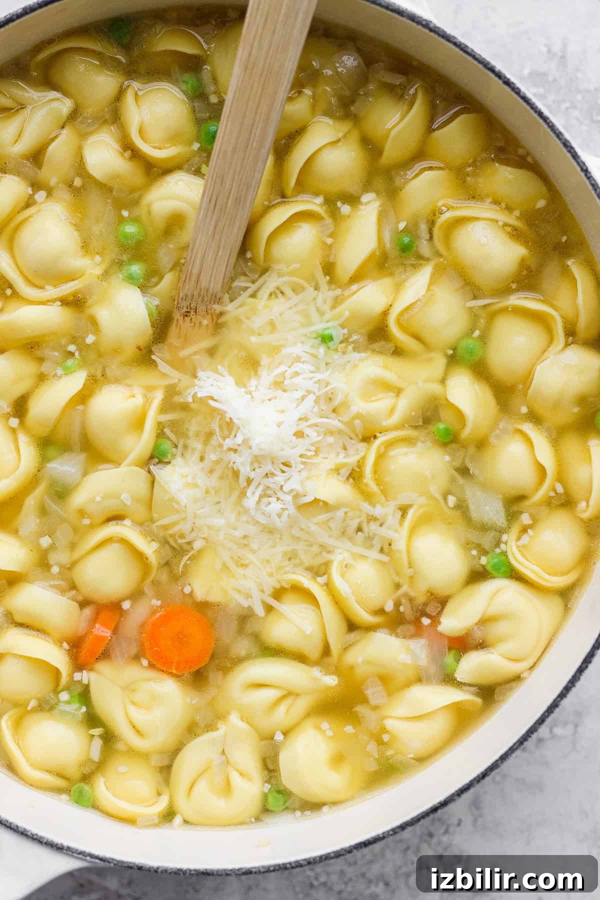 One-Pot Creamy Lemon Tortellini Soup with English Peas 5 A pot of tortellini soup with carrots, peas, and grated cheese on top.