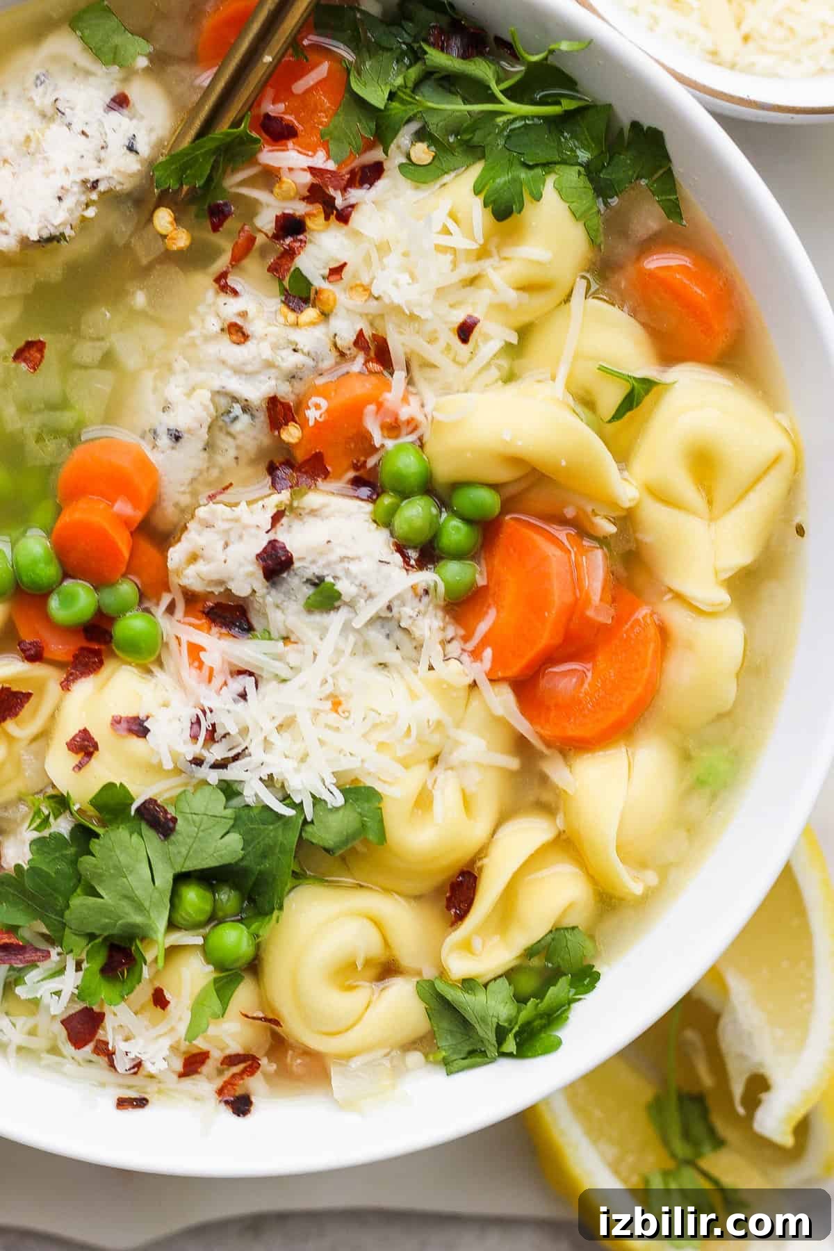 One-Pot Creamy Lemon Tortellini Soup with English Peas 8 A bowl of chicken noodle soup with vegetables, garnished with parsley and grated cheese.