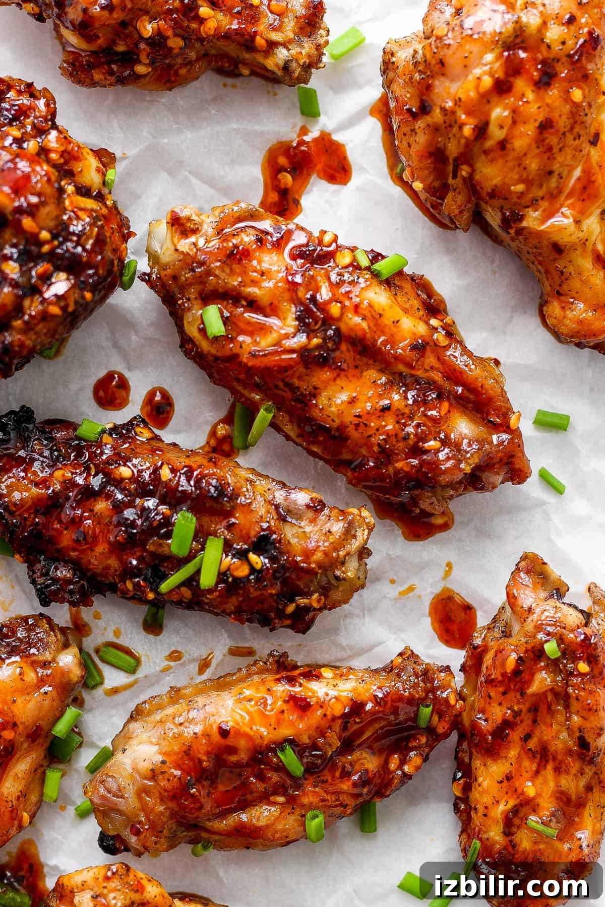 Glazed chicken wings sprinkled with sesame seeds and chopped green onions on parchment paper.
