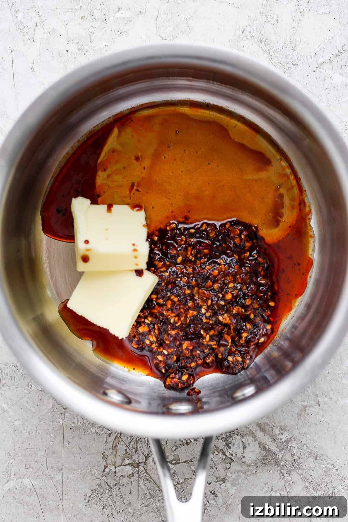 Ingredients in a saucepan including butter, chili flakes, and a dark liquid, possibly soy sauce or vinegar, preparing for a recipe.