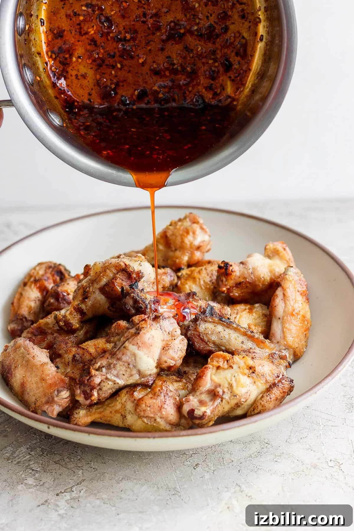 Pouring sauce over a plate of cooked chicken wings.