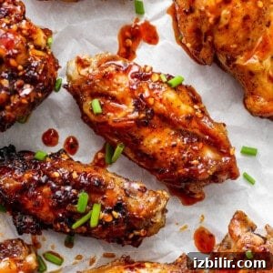 Glazed chicken wings on parchment paper garnished with sesame seeds and chopped green onions.
