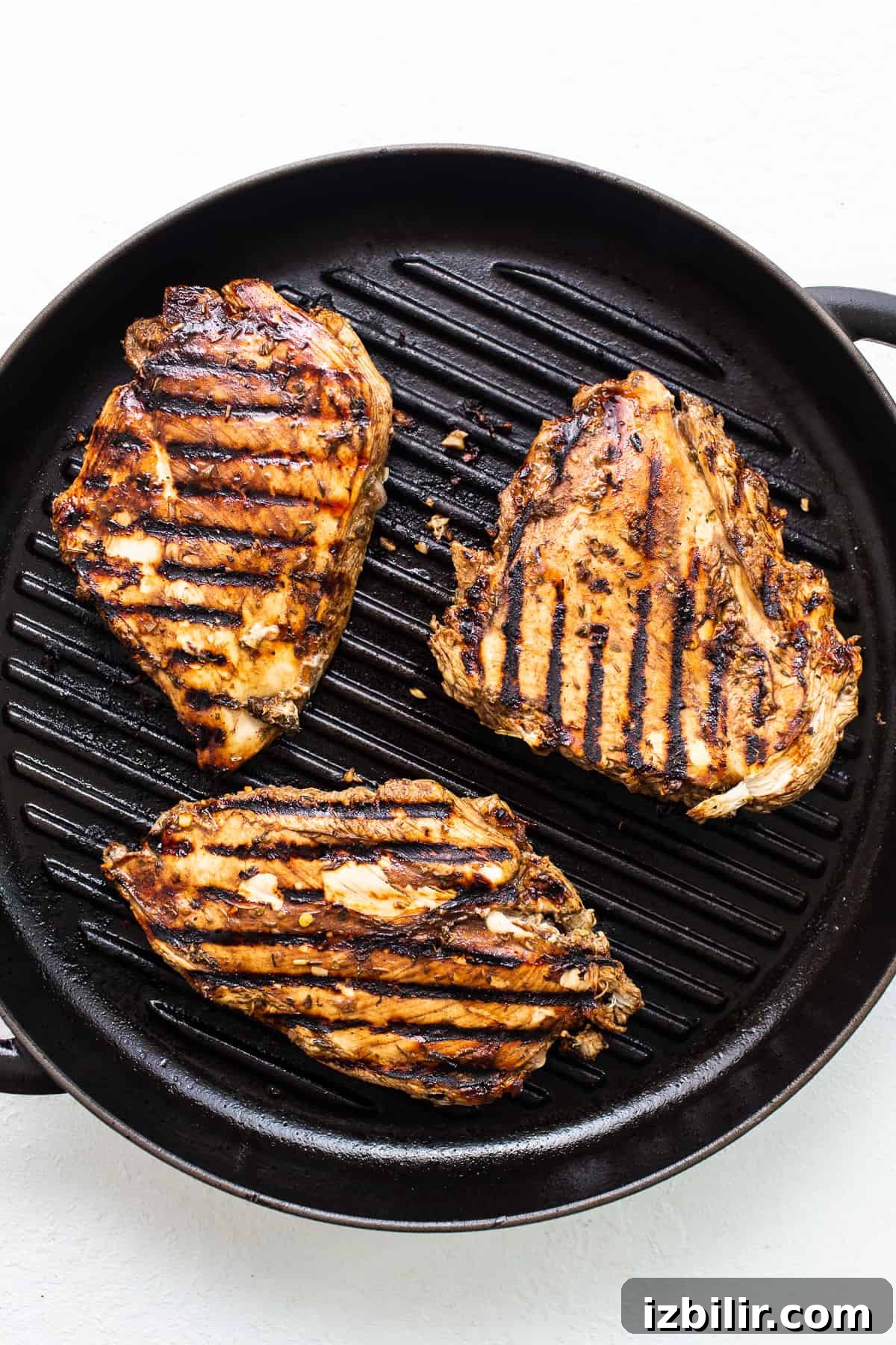 Grilled chicken breasts in a skillet on a white background.