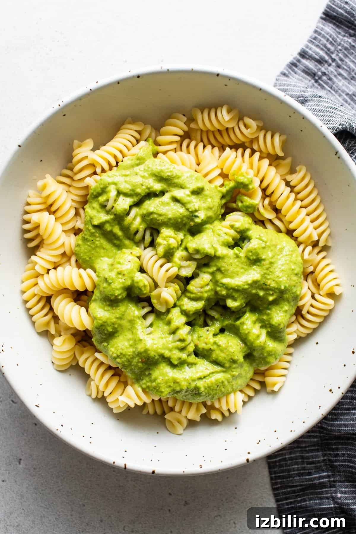 A bowl of rotini pasta topped with creamy green avocado sauce.