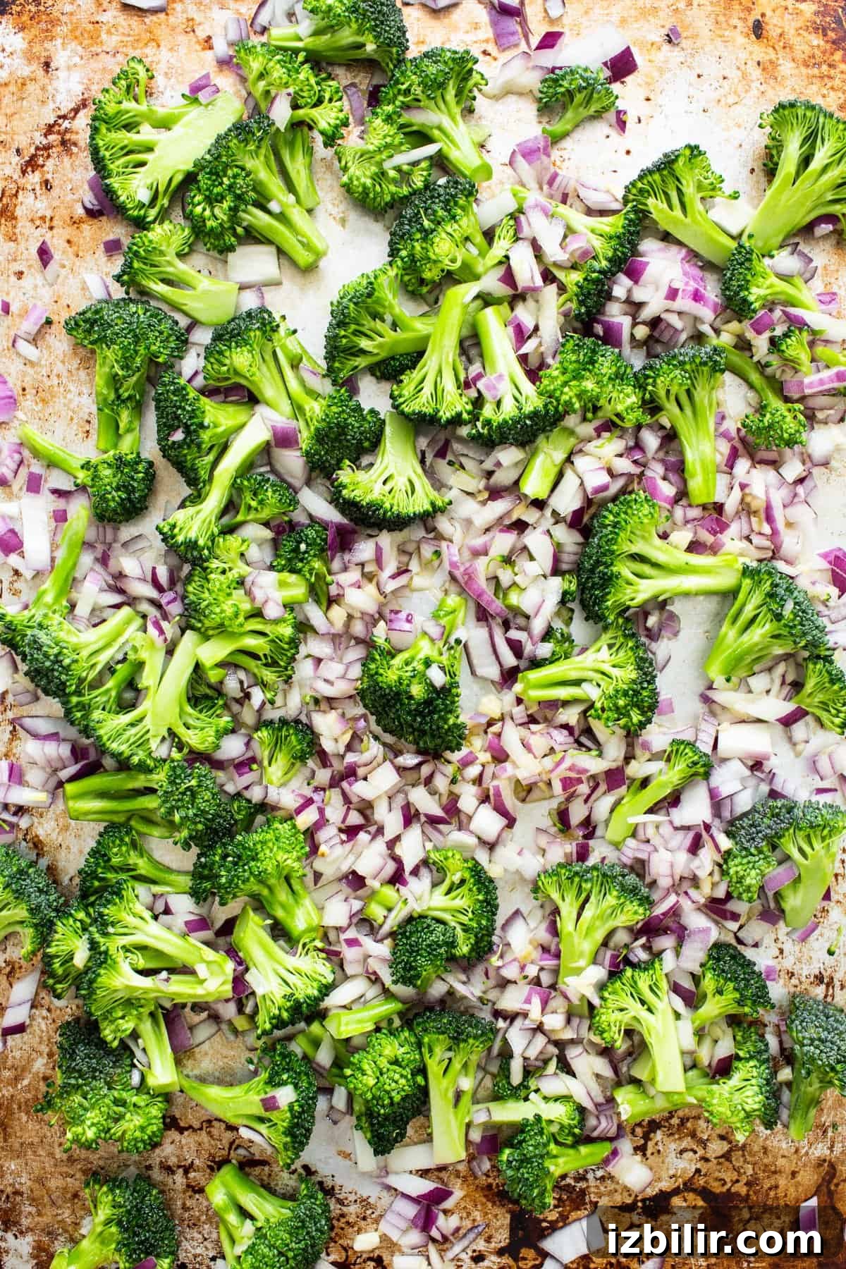 Chopped broccoli and red onions spread on a baking sheet, ready for roasting.