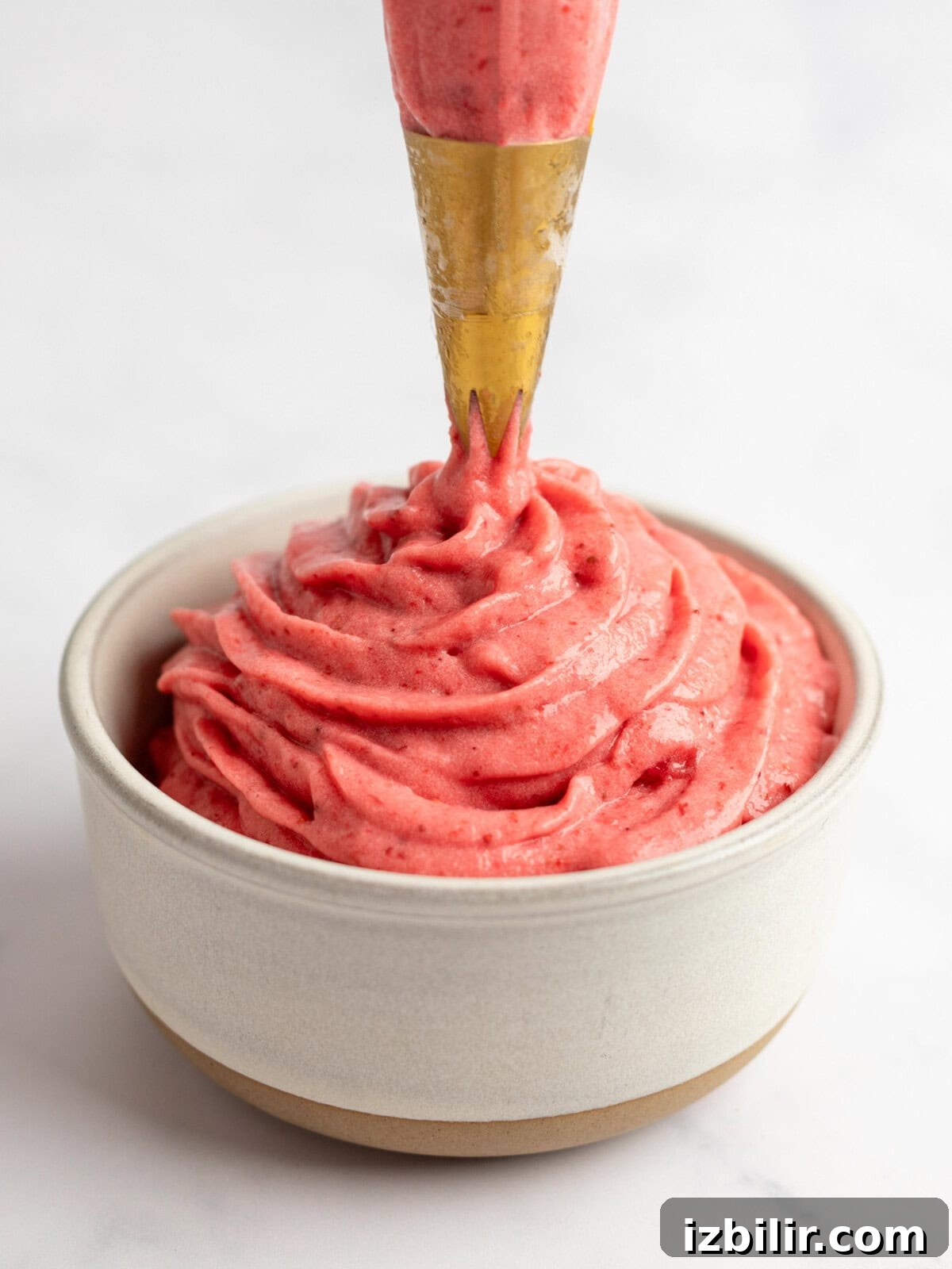 How to Make Strawberry Dole Whip: Dairy Free Soft Serve 6 A piping bag dispensing creamy strawberry frosting into a bowl.