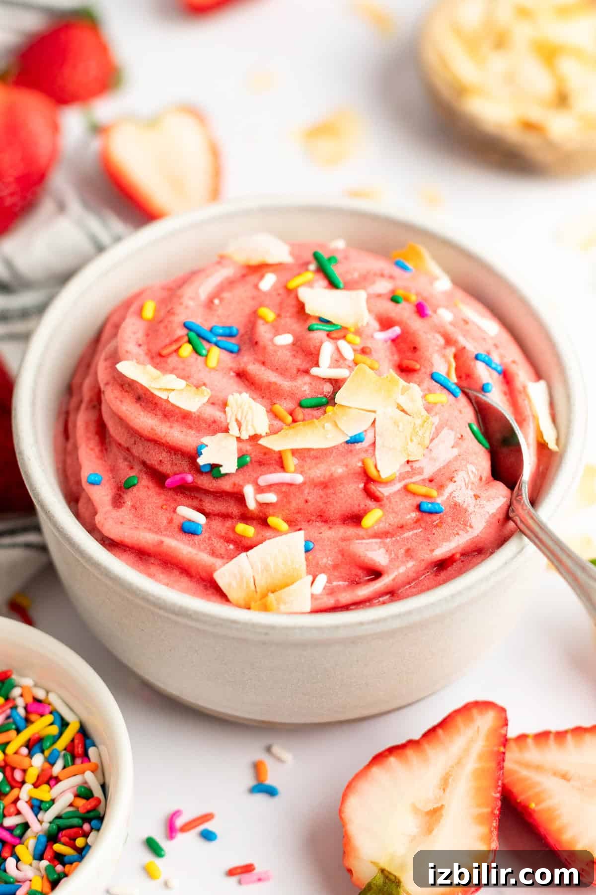 How to Make Strawberry Dole Whip: Dairy Free Soft Serve 7 A bowl of pink strawberry banana smoothie bowl topped with sprinkles and coconut flakes.