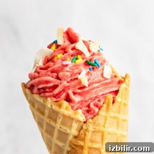 How to Make Strawberry Dole Whip: Dairy Free Soft Serve 8 A close-up of a strawberry soft serve ice cream cone topped with sprinkles and white chocolate chunks.