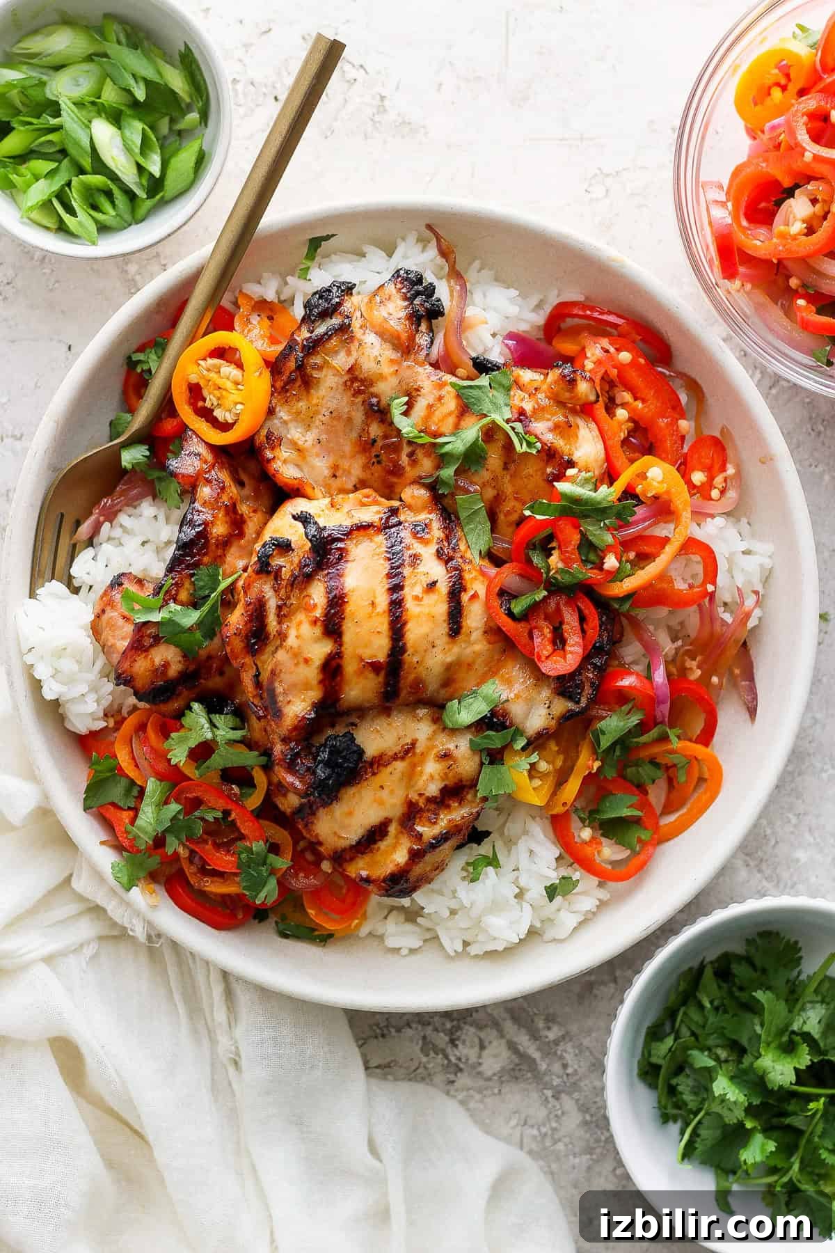Grilled Coconut Chicken Recipe with Lime Marinade 2 Grilled chicken thighs on a bed of white rice, garnished with sliced bell peppers, onions, and herbs in a bowl, with chopsticks on the side.
