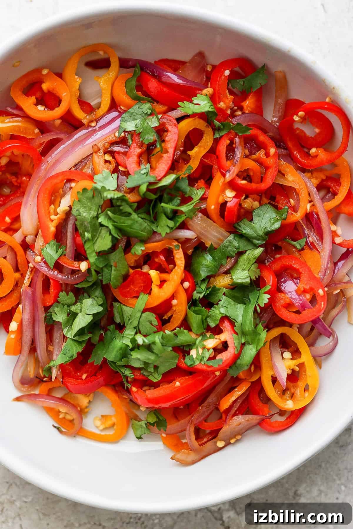 Grilled Coconut Chicken Recipe with Lime Marinade 5 A bowl of sliced red onions, red and orange bell peppers, garnished with fresh cilantro.