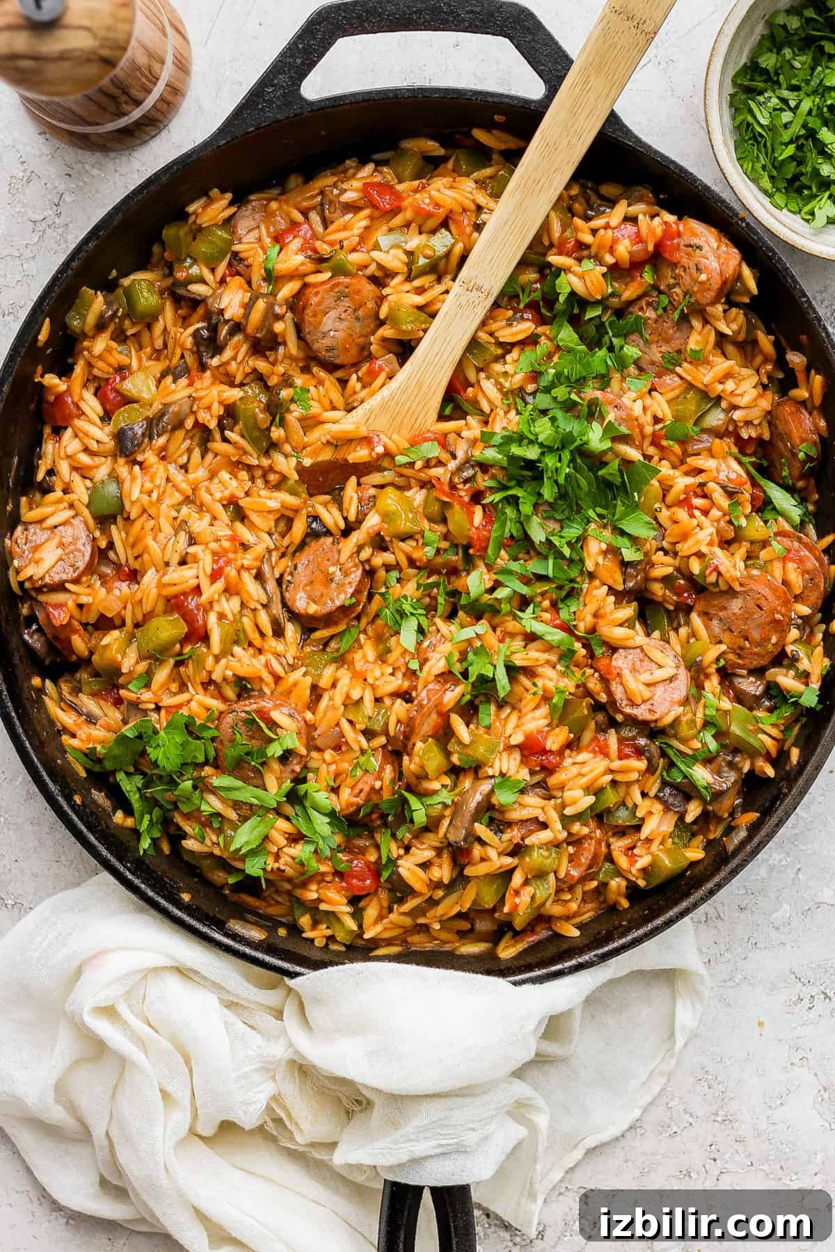 A skillet full of rice and vegetables with a wooden spoon.