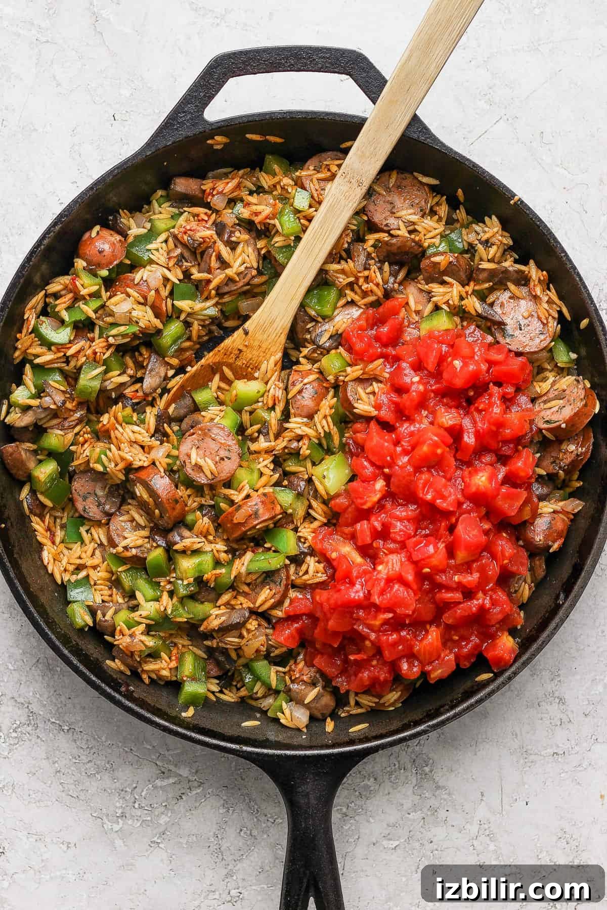 A skillet full of rice and meat with a wooden spoon.