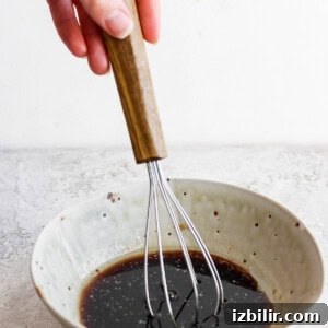 Savory Mixed Protein Bowl with Grains and Veggies 11 A hand whisking a liquid mixture in a ceramic bowl.