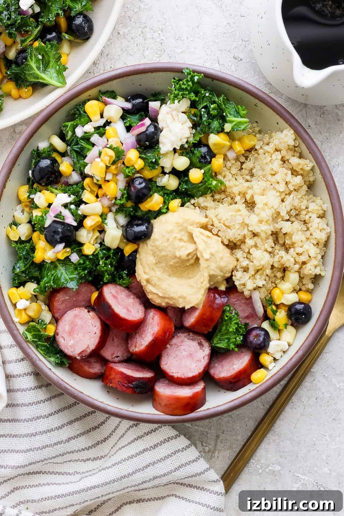 Savory Mixed Protein Bowl with Grains and Veggies 6 A bowl of quinoa, sliced sausage, and mixed vegetables, topped with a dollop of hummus.