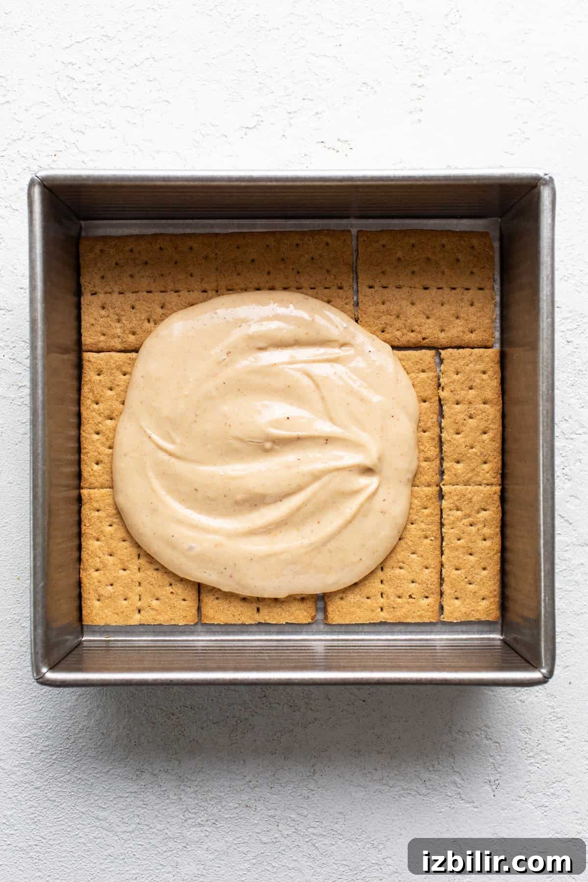 A square baking dish filled with graham crackers topped with a layer of smooth, creamy filling.