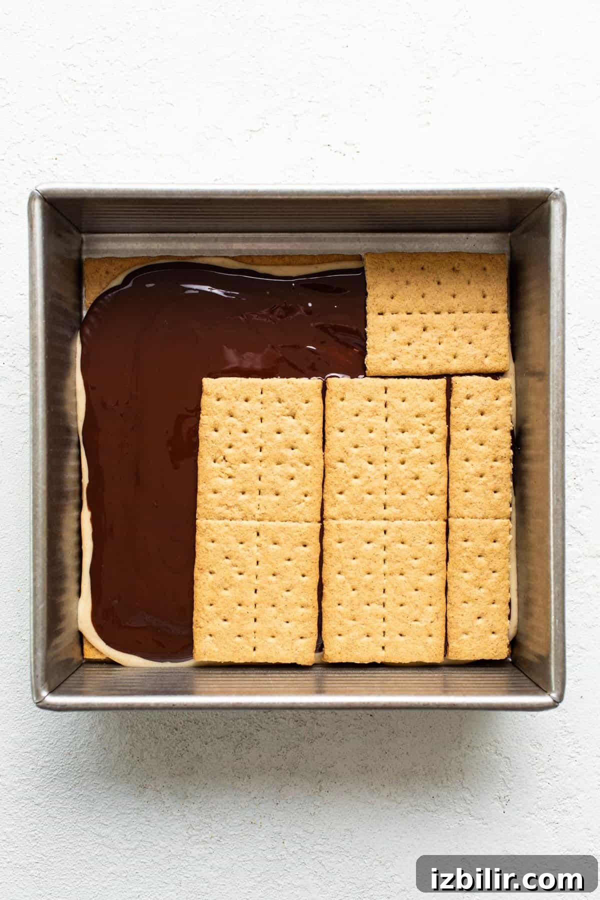 A baking dish with a layer of chocolate topped by aligned graham crackers, preparing for a s'mores dessert.