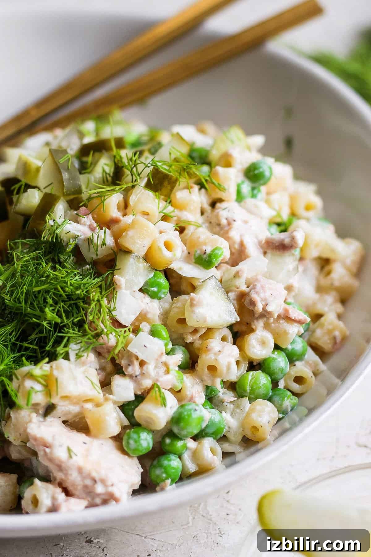 Creamy Dill Tuna Pasta Salad Recipe 5 A bowl of tuna pasta salad with peas and dill, garnished with fresh herbs and served with chopsticks.