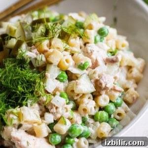 Creamy Dill Tuna Pasta Salad Recipe 6 A bowl of pasta salad with peas, diced pickles, chunks of chicken, and fresh dill on top.