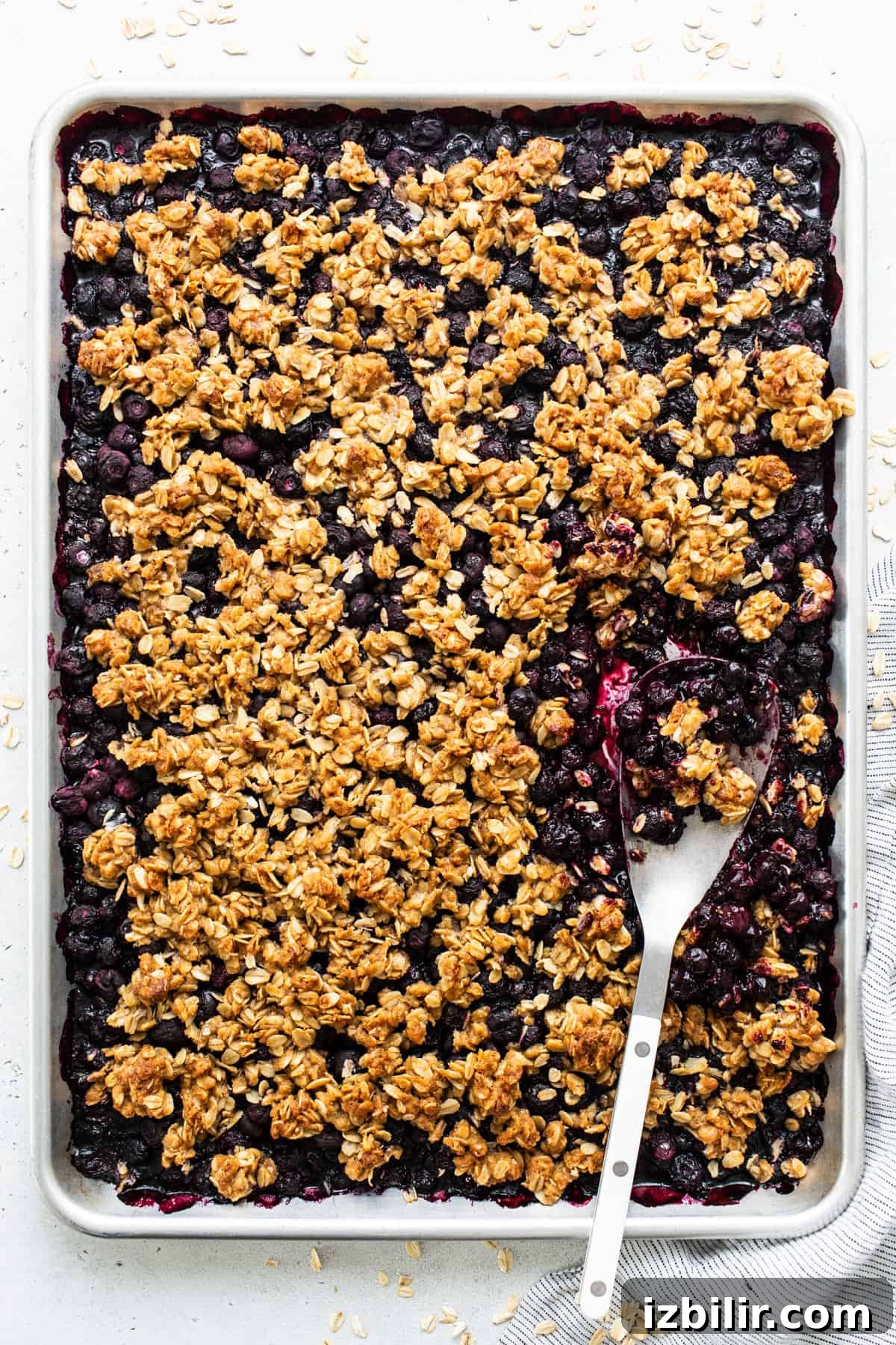 Sheet Pan Blueberry Crisp Recipe 4 A baked blueberry oatmeal crumble in a rectangular pan with a serving spoon.