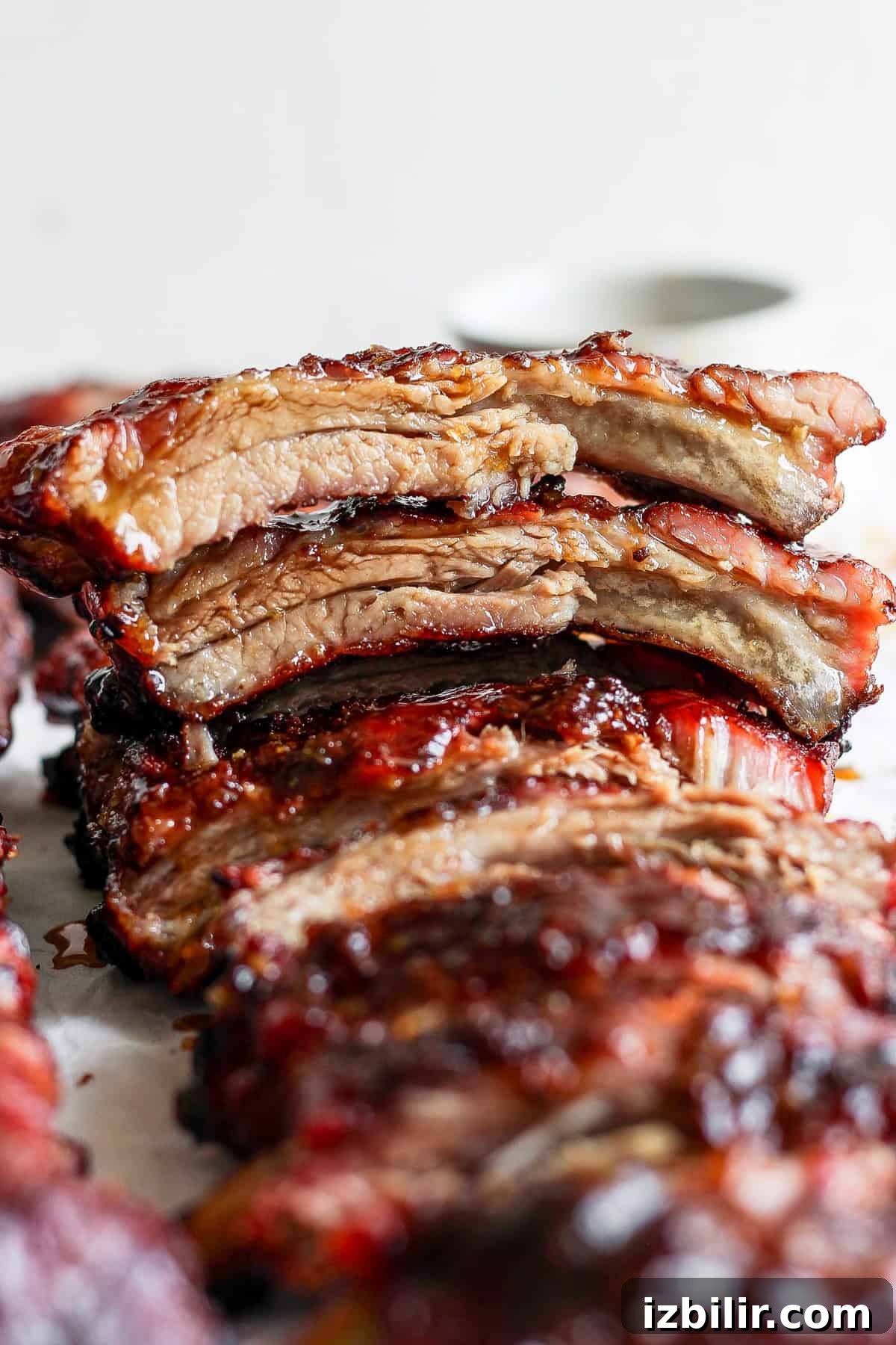 Close-up of a stack of glazed, grilled ribs, with the top piece cut to show a juicy, tender interior. The meat is richly caramelized with a glossy, charred exterior.
