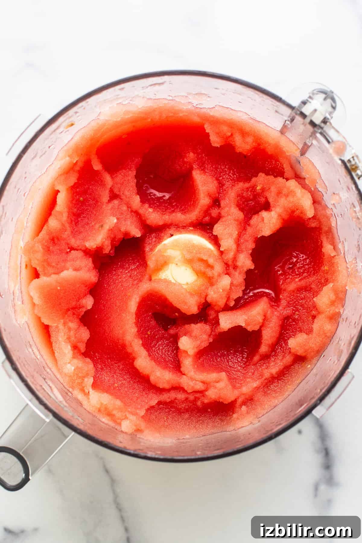 Top view of a blender filled with blended watermelon, showcasing a vivid red mixture with a swirling texture.