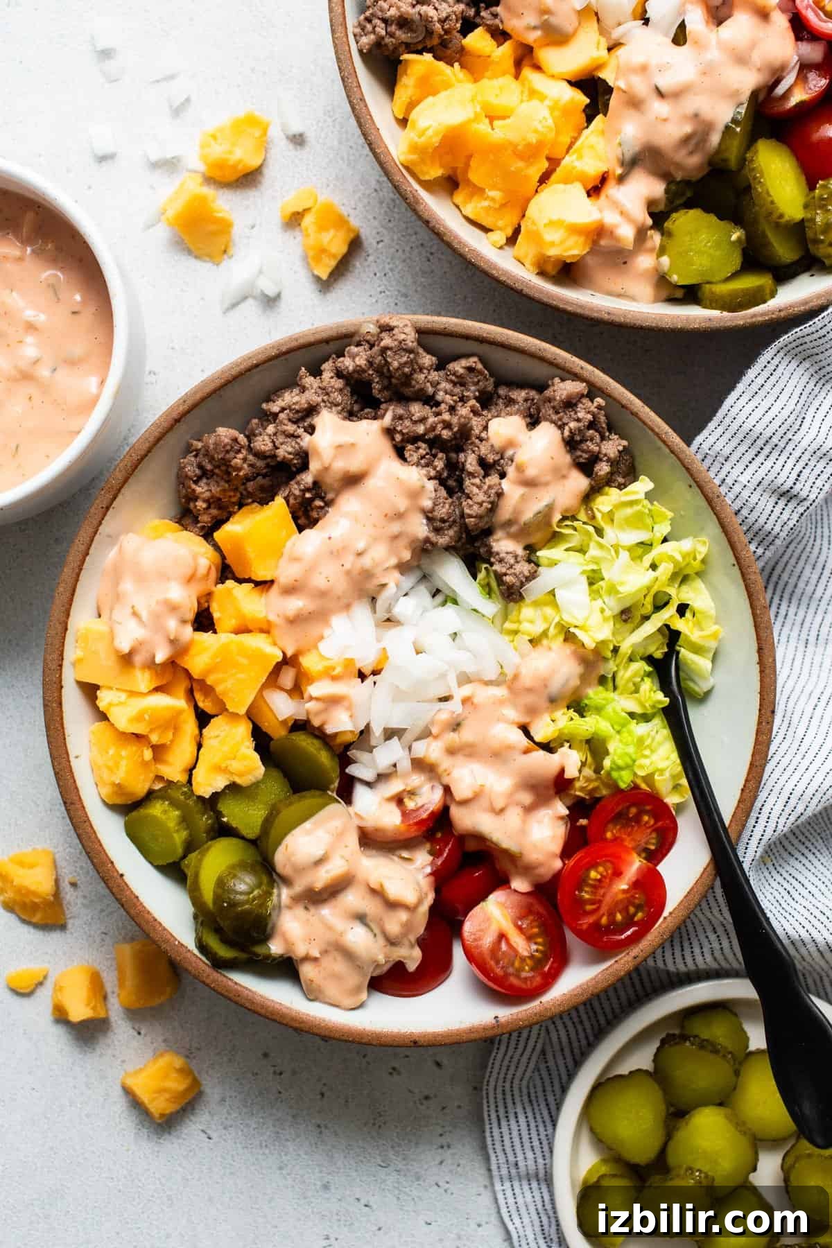 A bowl of salad with ground beef, rice, lettuce, tomatoes, pickles, olives, and diced mango, topped with a creamy dressing.